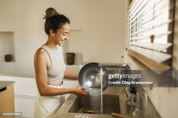 cheerful smiling woman washing dishes on kitchen. household chores with pleasure - wash the dishes stockfoto's en -beelden
