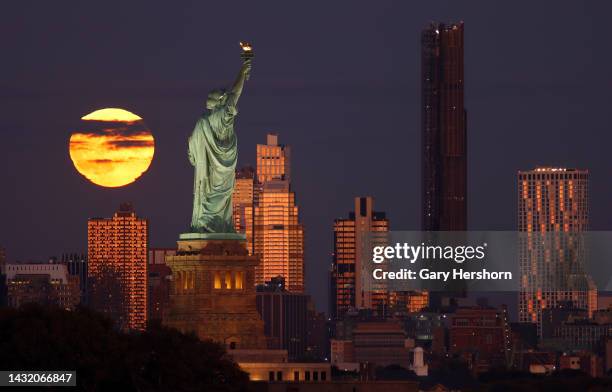 The full Hunter's Moon rises behind the skyline of Brooklyn, the Statue of Liberty and the Brooklyn Tower as the sun sets in New York City on October...