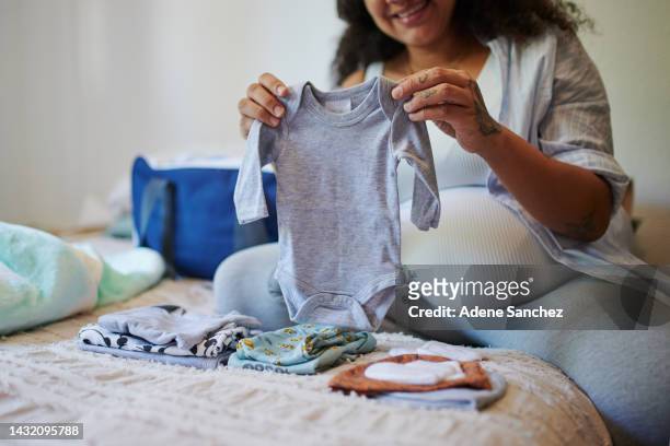 pregnant, woman and baby or newborn clothes being fold  or packed for due date while in bedroom. pregnancy, mother and female excited for arrival of child and packing checklist baby items in bag. - baby bag stockfoto's en -beelden