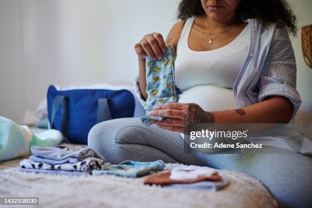 clothes, packing and woman pregnant with baby prepare for newborn child or kid while relax in home bedroom. love, pregnancy and expectation for maternity girl, mother or mom with fresh laundry outfit - baby clothing stock pictures, royalty-free photos & images