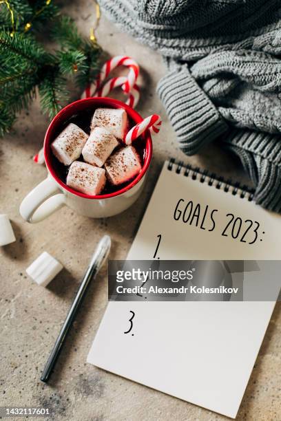 hot chocolate with marshmallows and candy cane and open note pad with new year 2023 goals list. planning goals for the next year - christmas list stock-fotos und bilder