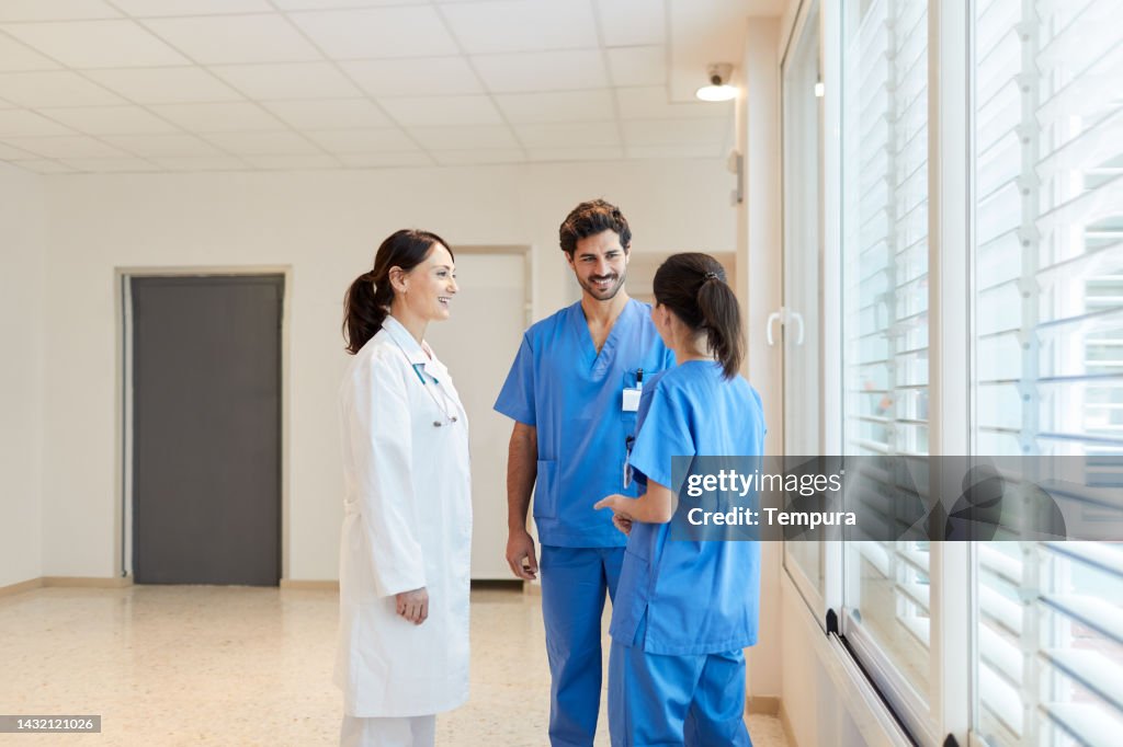 Entspanntes Gespräch von medizinischem Personal, das an Fenstern im Krankenhauskorridor steht
