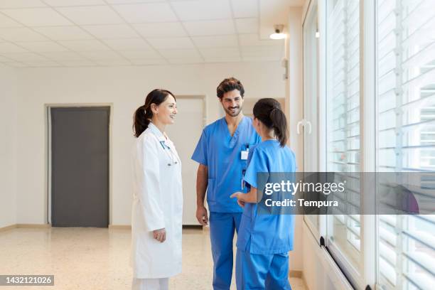entspanntes gespräch von medizinischem personal, das an fenstern im krankenhauskorridor steht - krankenpfleger stock-fotos und bilder