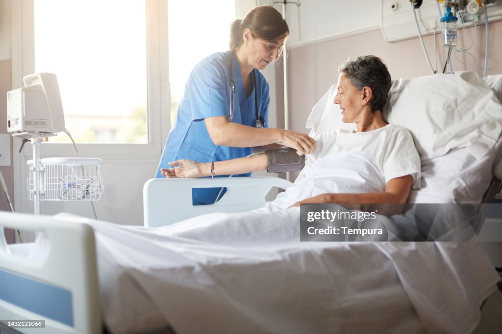 Krankenschwester stellt das Blutdruckmessgerät auf weibliche Krankenhauspatientin ein