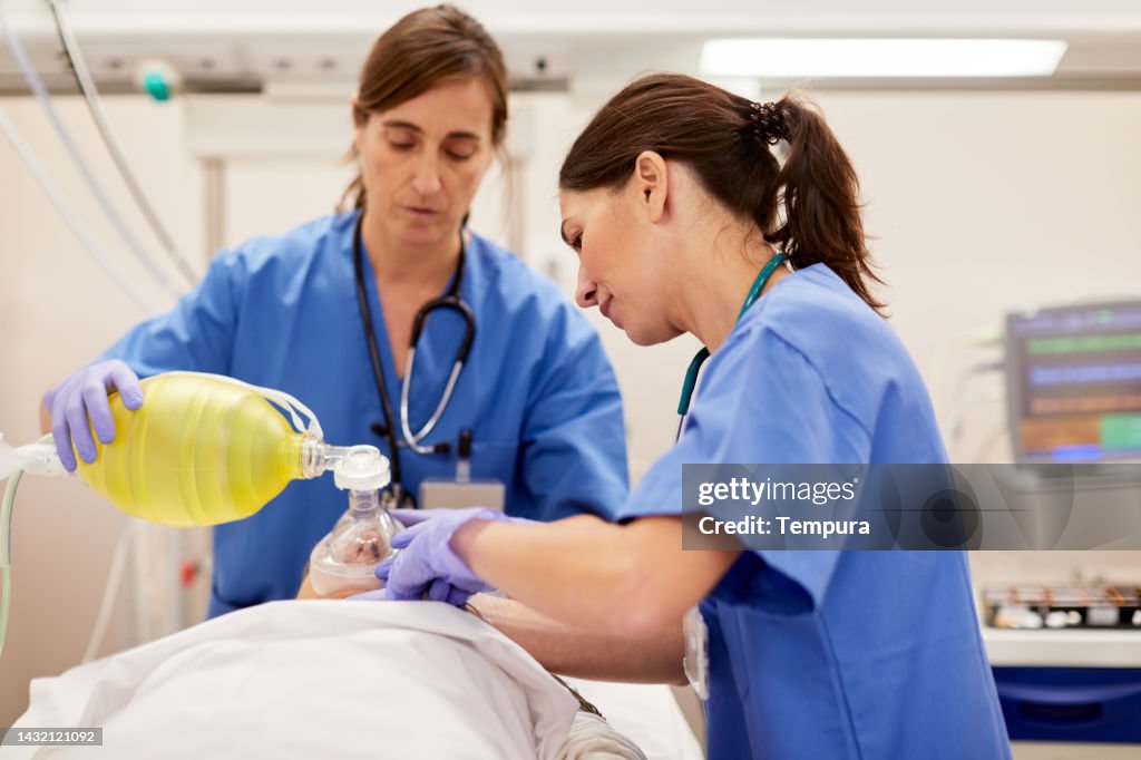 Medical staff are bagging a patient, i.e., providing positive pressure ventilation to a patient with a bag valve mask (BVM)