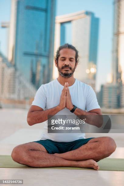 man praying in easy pose with eyes closed, yoga practice for relaxation - yoga office arab stock pictures, royalty-free photos & images