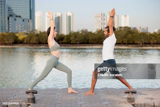 man and woman doing yoga for relaxation together on the pier in abu dhabi - warrior position stock pictures, royalty-free photos & images