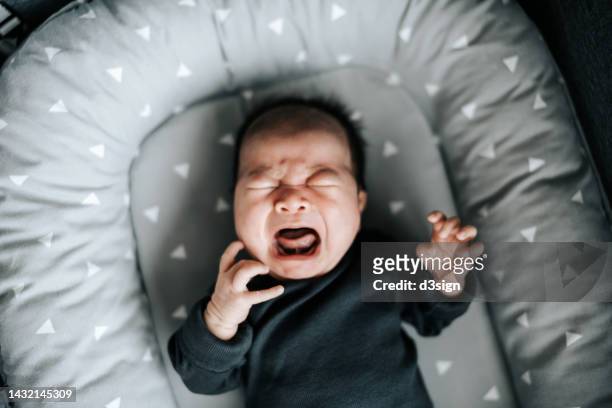 high angle shot of asian newborn baby girl crying in the crib at home. hunger and discomfort - huilen stockfoto's en -beelden