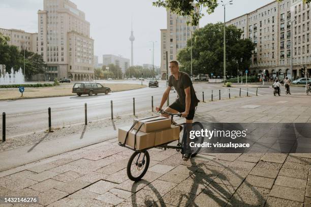 delivery man riding with loaded cargo bike - cargo bike stock pictures, royalty-free photos & images