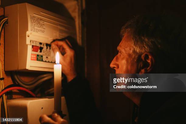 停電時にキャンドルライトでホームヒューズボックスをチェックする高齢者 - electrical fuse ストックフォトと画像