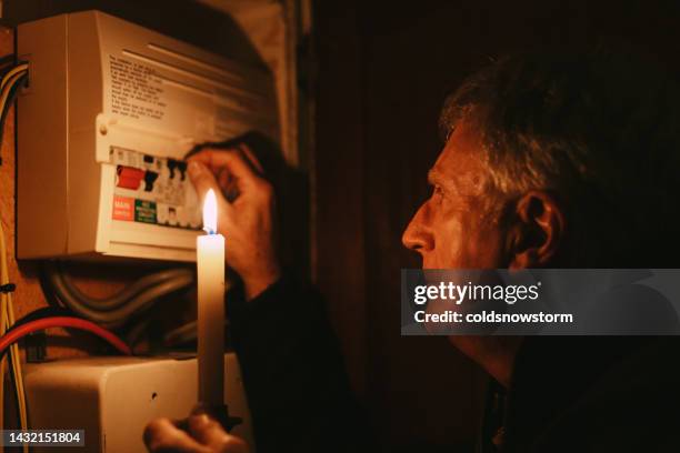 senior man checking home fuse box by candlelight during power outage - apagão imagens e fotografias de stock