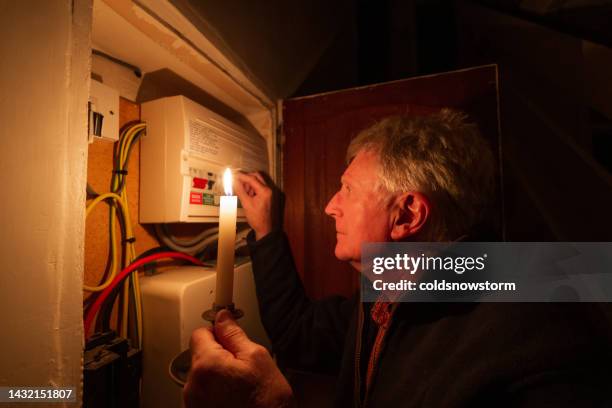 senior man checking home fuse box by candlelight during power outage - uk plug socket stock pictures, royalty-free photos & images