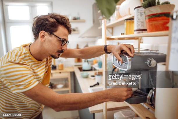 giovane uomo vestito casualmente che prepara il caffè nella sua cucina domestica - caffettiera foto e immagini stock