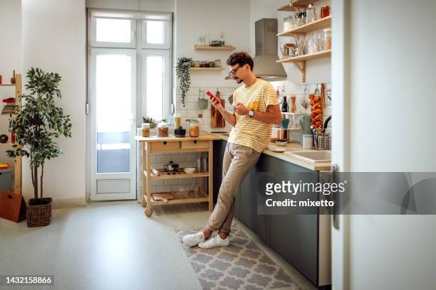 shot of a young man using a cellphone in the kitchen at home - one man only stock pictures, royalty-free photos & images
