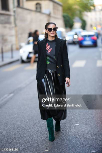 Olivia Palermo wears black sunglasses, earrings, a diamonds necklace, a black with embroidered red and green leaves pullover, a black shoulder-pads...
