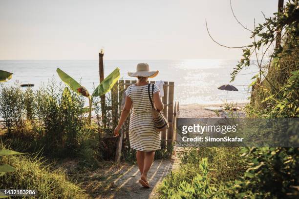 woman wearing hat walking amidst plants towards beach during sunny day - albania stock pictures, royalty-free photos & images