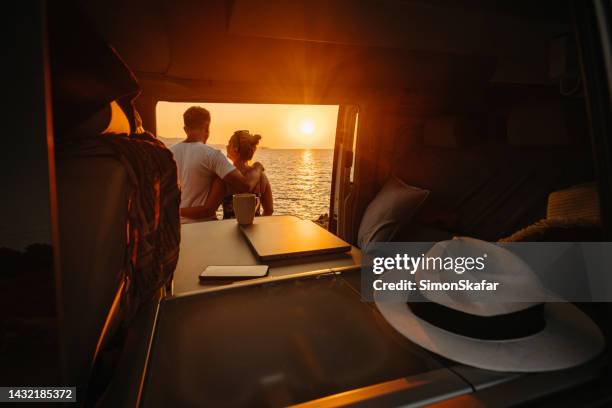 couple enjoying sunset over sea while standing together outside camper trailer - sea cup stock pictures, royalty-free photos & images