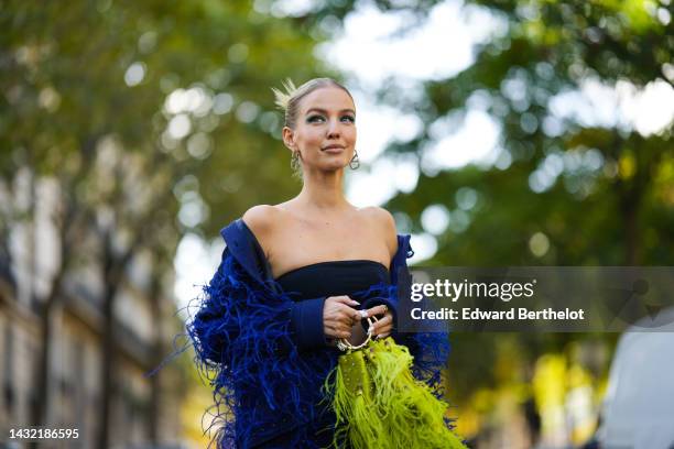 Leonie Hanne wears a black shoulder-off top, a navy blue with royal blue embroidered feathers / felt wool jacket from Elie Saab, a matching royal...