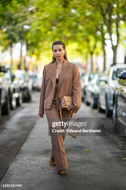 Julia Comil wears gold earrings, a brown with black checkered print pattern oversized jacket, a gold necklace, matching brown with black checkered...