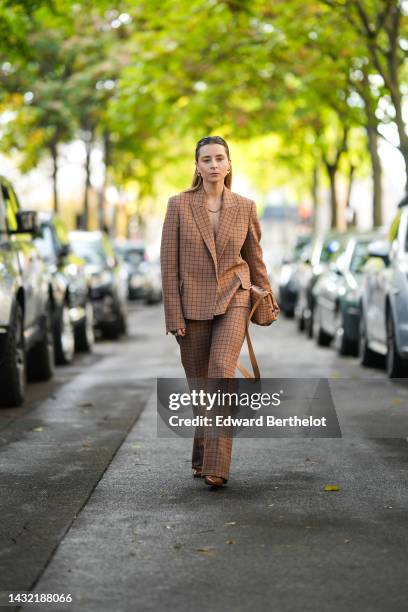 Julia Comil wears gold earrings, a brown with black checkered print pattern oversized jacket, a gold necklace, matching brown with black checkered...