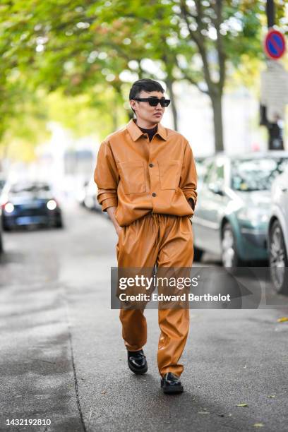 Jeck Aguilar wears black sunglasses, a black t-shirt, a camel shiny leather shirt, matching camel shiny leather large pants, a gold Love bracelet...