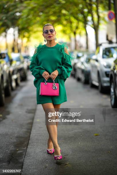 Olga Ferrara wears black circle sunglasses, silver rhinestones fringed earrings, a green cut-out shoulder / embroidered feather / embroidered...