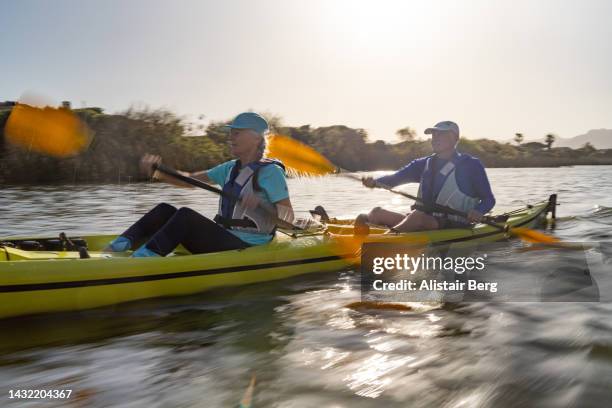 senior couple kayaking on a lake together at sunset - seniors canoeing stock pictures, royalty-free photos & images