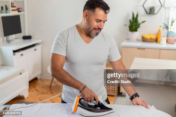 um homem em casa passando o botão para baixo da camisa. - gender role - fotografias e filmes do acervo