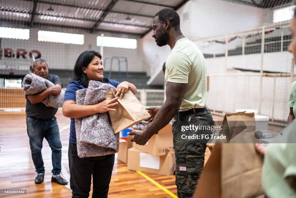 Mature woman receiving food and blanket from a soldier at a community center