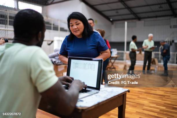 freiwilliger spricht mit einer flüchtlingsfrau, während er den laptop in einer flüchtlingsunterkunft benutzt - notunterkunft stock-fotos und bilder