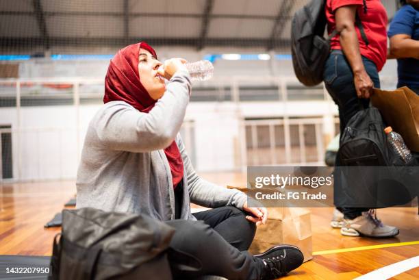 refugee woman wearing hijab drinking water in a sheltering - red cross stock pictures, royalty-free photos & images