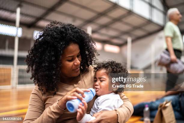 refugee mother feeding her baby in a sheltering at a community center - african refugee stock pictures, royalty-free photos & images