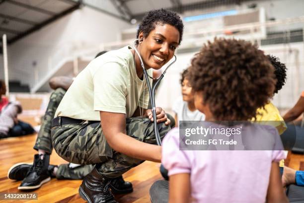 army doctor examining refugee children at a community center - army soldier smiling stock pictures, royalty-free photos & images