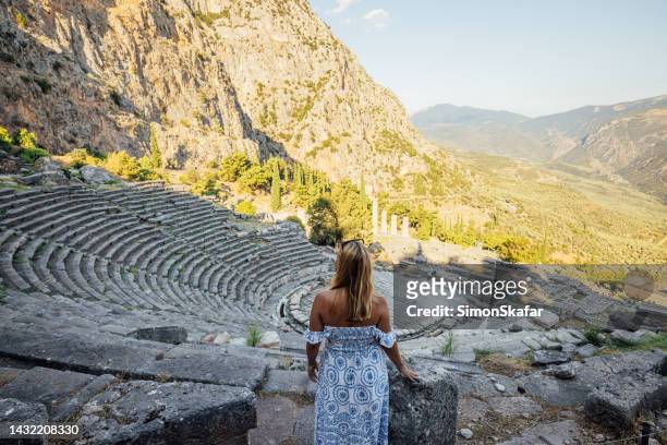 female tourist exploring old ruins of greek amphitheatre against mountains - delphi stock pictures, royalty-free photos & images