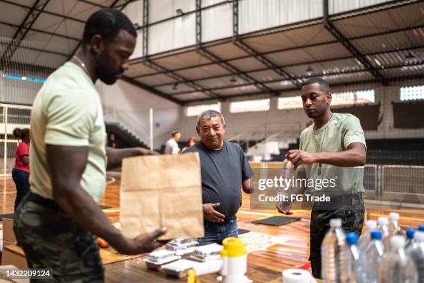 soldiers giving food to a disabled mature man at a community center - distribution center stockfoto's en -beelden