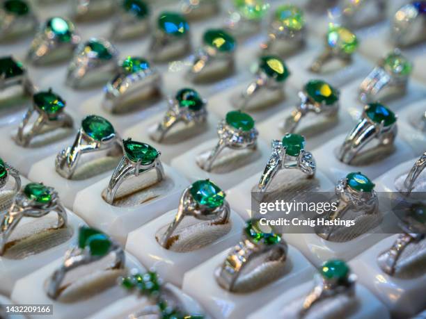 emerald coloured gemstone set rings arranged in a row in jewellery store shop setting. luxury ring display with shining colourful stones and diamonds. high end luxury shopping. - smaragdgroen stockfoto's en -beelden