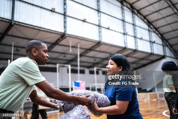 reife frau erhält eine decke von einem soldaten in einer turnhalle - humanitarian aid stock-fotos und bilder