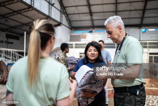 soldier with a clipboard giving donations to refugees in a sheltering - homeless shelter stock pictures, royalty-free photos & images