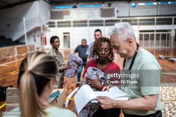 soldier with a clipboard giving donations to refugees in a sheltering - sheltering stock pictures, royalty-free photos & images