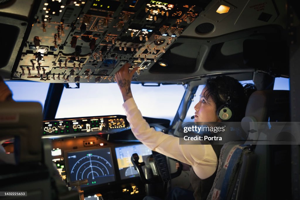 Rückansicht einer Pilotin, die während des Flugzeugflugs Schalter einstellt