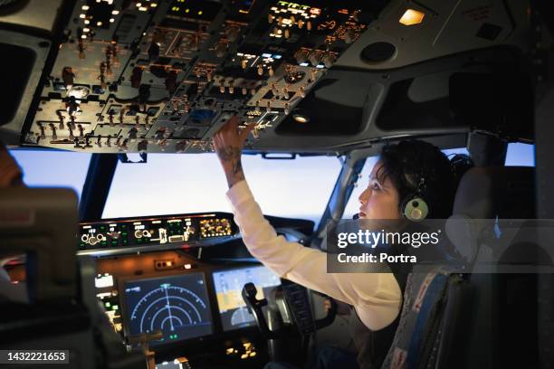 vista posteriore di una donna pilota che regola gli interruttori durante il volo dell'aeroplano - navigator foto e immagini stock