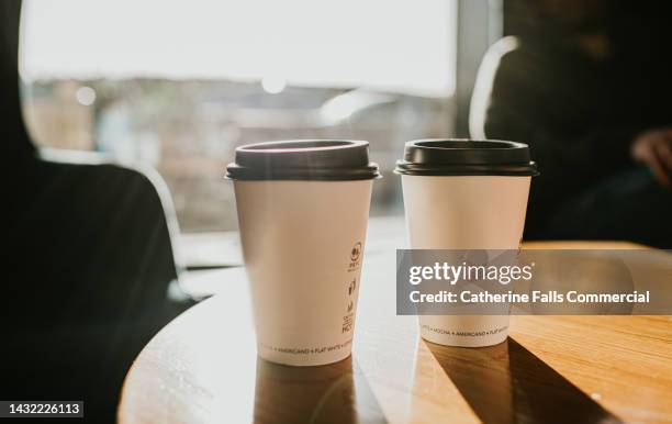 takeaway coffee cups on a wooden table casting long shadows - einmalprodukt stock-fotos und bilder
