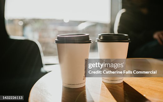 Takeaway coffee cups on a wooden table casting long shadows Takeaway coffee cups on a wooden table casting long shadows