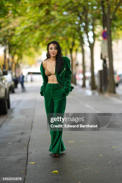 Jessica Wang wears gold earrings, a gold lips ring, a gold glitter bra underwear, a dark green velvet zipper jacket, a dark green velvet large pants,...