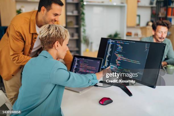 smiling male programmer explains a coding technique to a new female colleague while sitting at a desk in the office - java stockfoto's en -beelden