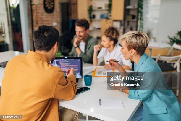 a male programmer shows a female colleague a coding technique. the codes are visible on the laptop screen - webdesigner stockfoto's en -beelden