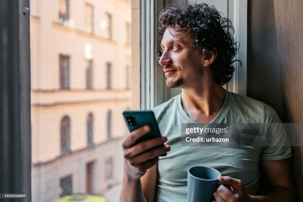 Young Man Drinking Coffee And Using Phone Indoors