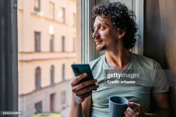 young man drinking coffee and using phone indoors - men stock pictures, royalty-free photos & images