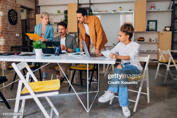 a young hispanic woman is learning to code on a laptop computer in the office, while her colleagues study in the team - html css stock pictures, royalty-free photos & images
