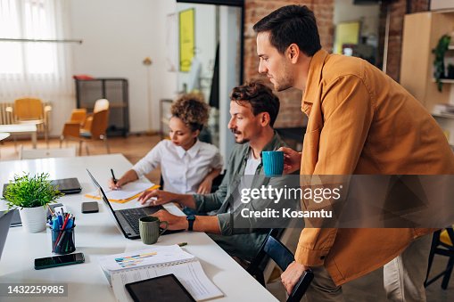 Two students learn coding techniques using a laptop and take notes while being guided by an IT expert Two students learn coding techniques using a laptop and take notes while being guided by an IT expert